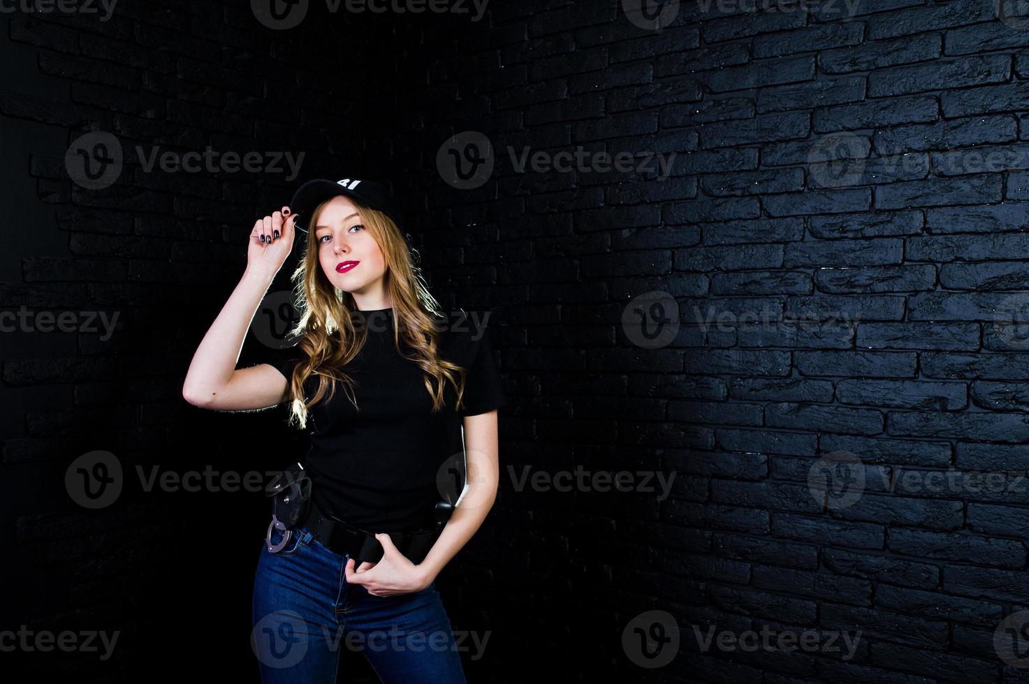 FBI female agent in cap and with gun at studio against dark brick wall. photo