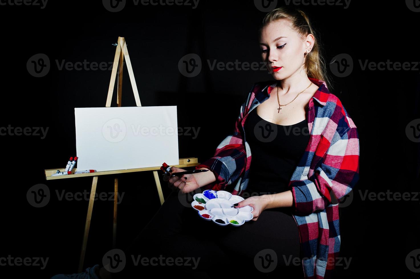 Beautiful woman artist painter with brushes and oil canvas posing in studio isolated on black. photo