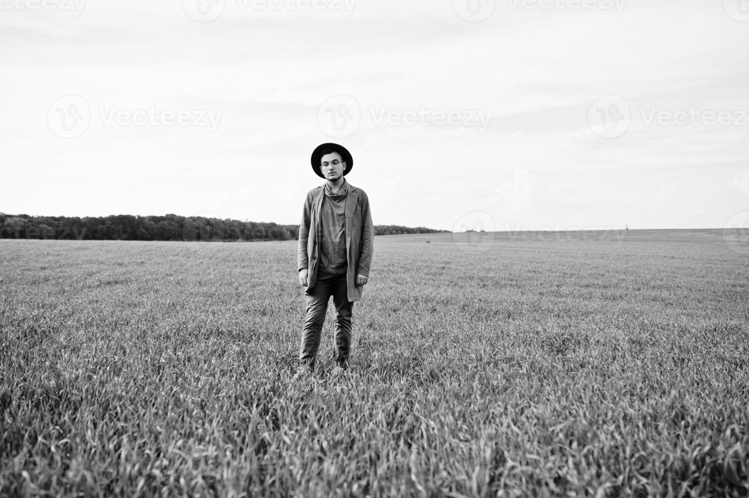 hombre elegante con gafas, chaqueta marrón y sombrero posado en campo verde. foto