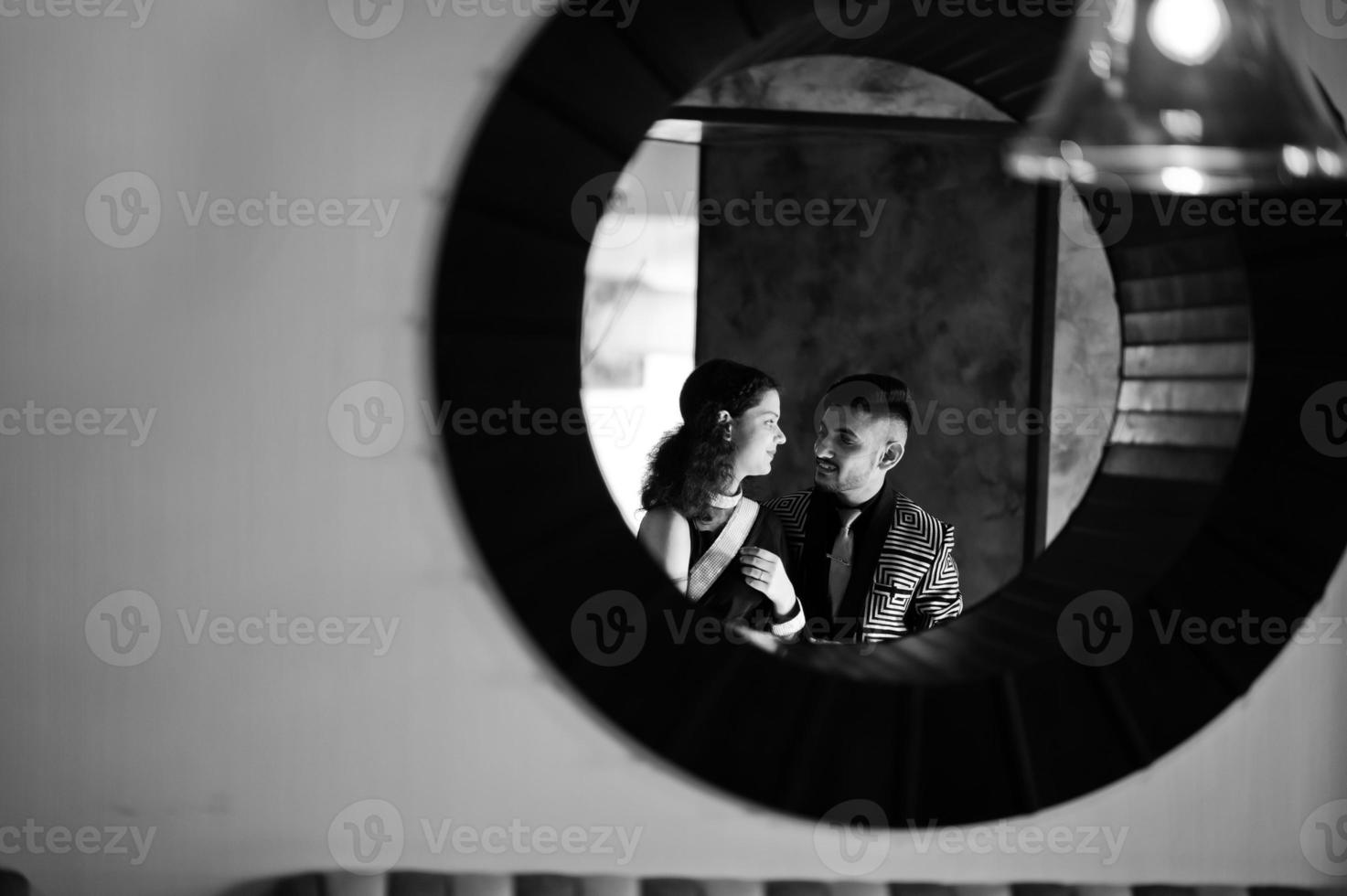 Lovely indian couple in love, wear at saree and elegant suit, posed on restaurant at round circle at wall. photo