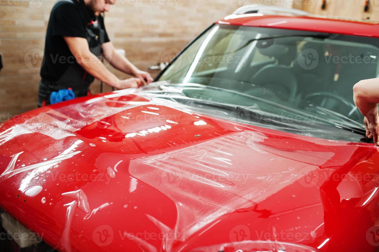 Car service worker put anti gravel film on a red car body at the detailing vehicle workshop. Car protection with special films. photo