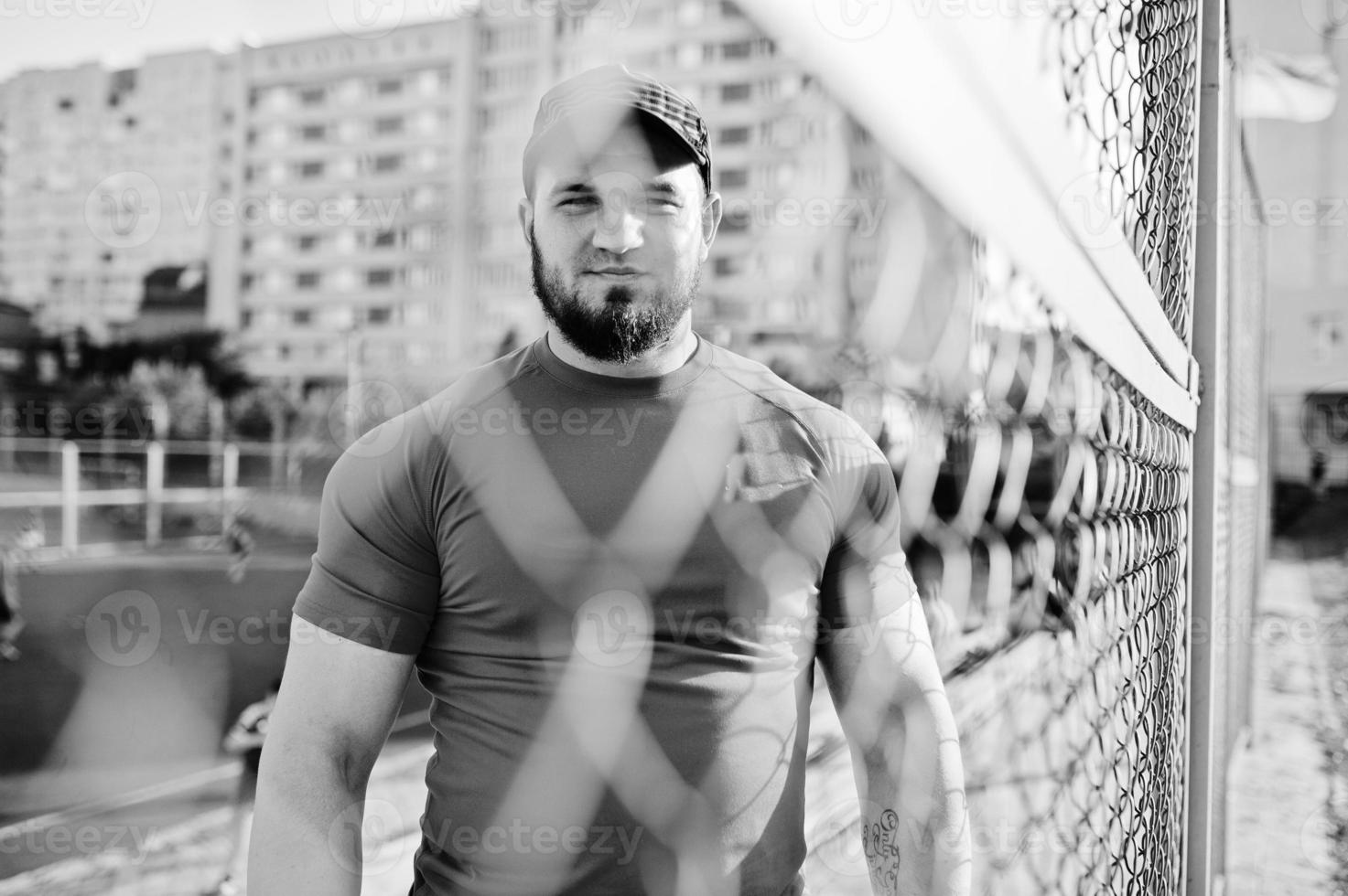 Young brutal bearded muscular man wear on red shirt, shorts and cap at stadium. photo