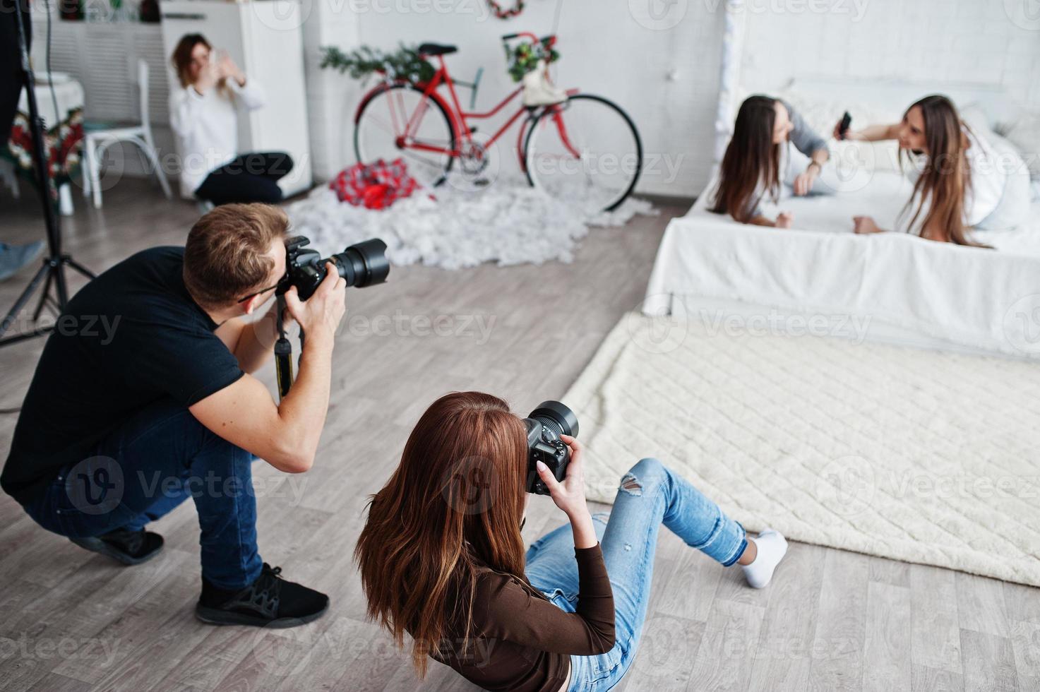 el equipo de dos fotógrafos fotografiando a chicas gemelas en el estudio. fotógrafo profesional en el trabajo. foto