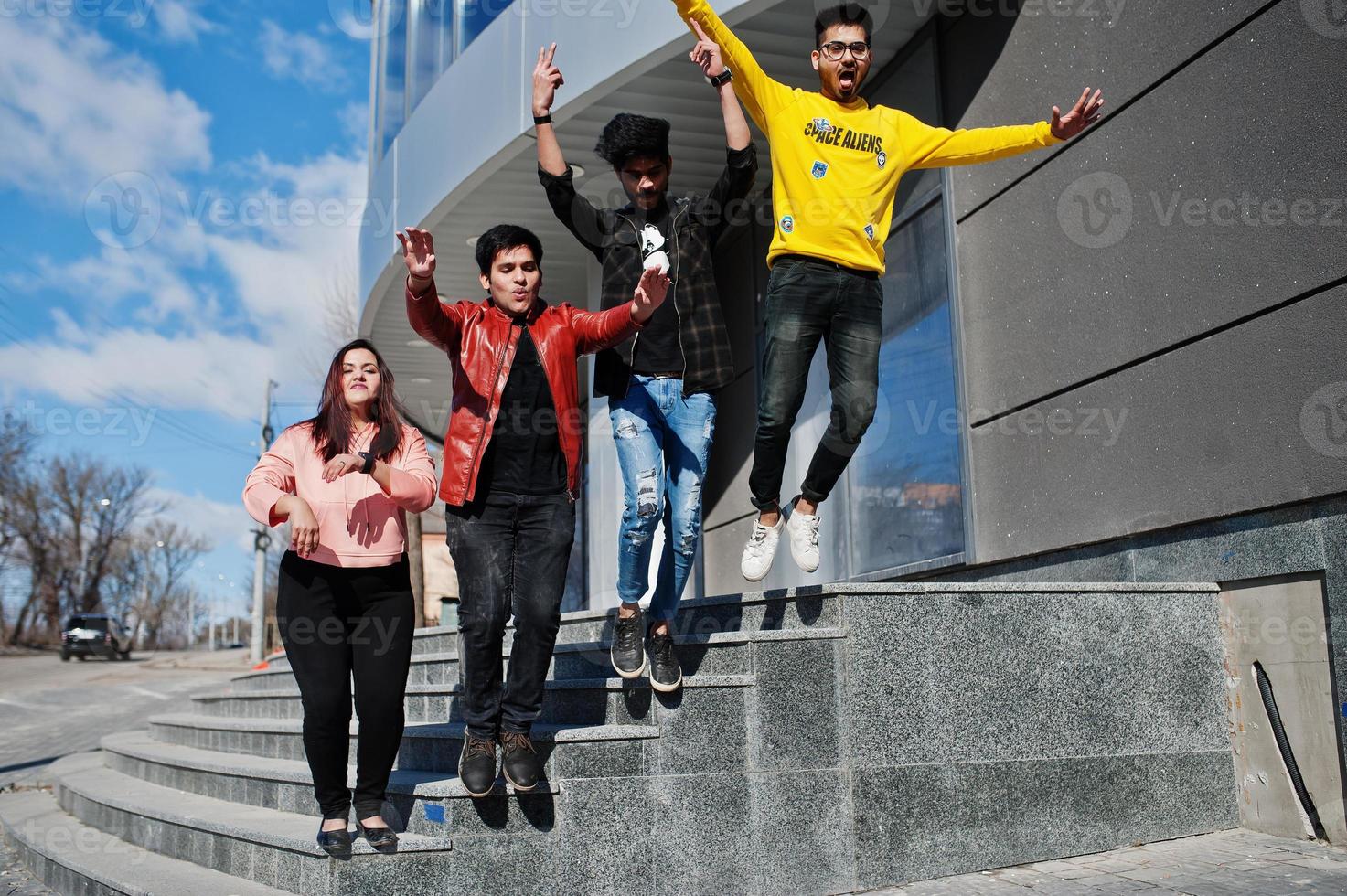 un grupo de amigos asiáticos se paran en las escaleras al aire libre contra un edificio moderno y saltan juntos. foto