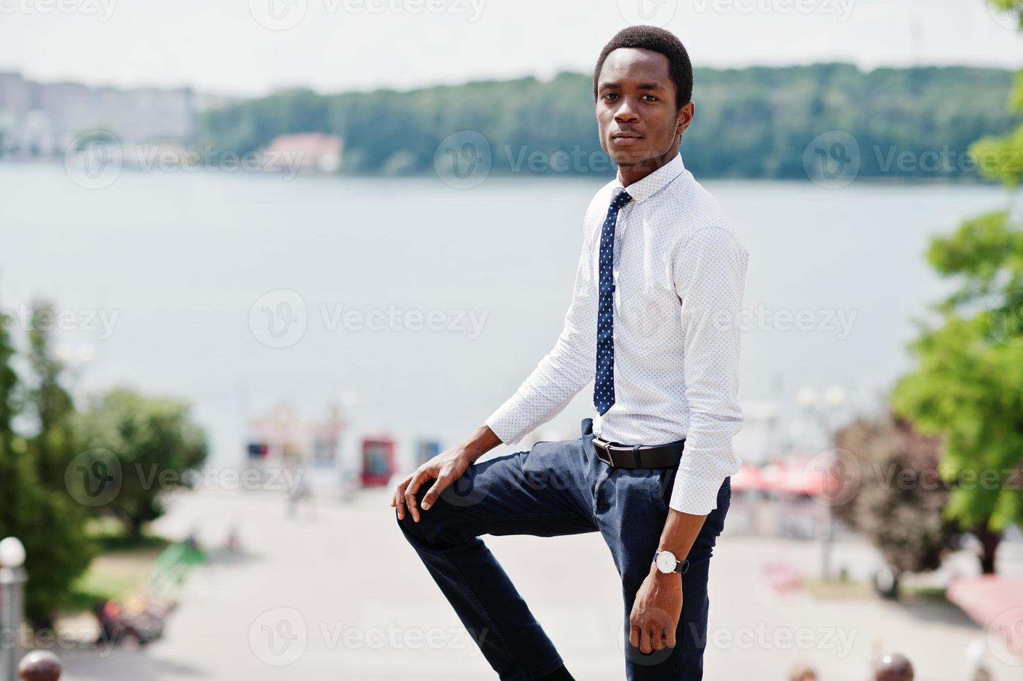 Stylish african american business man at pants and shirt posed outdoor against lake. photo