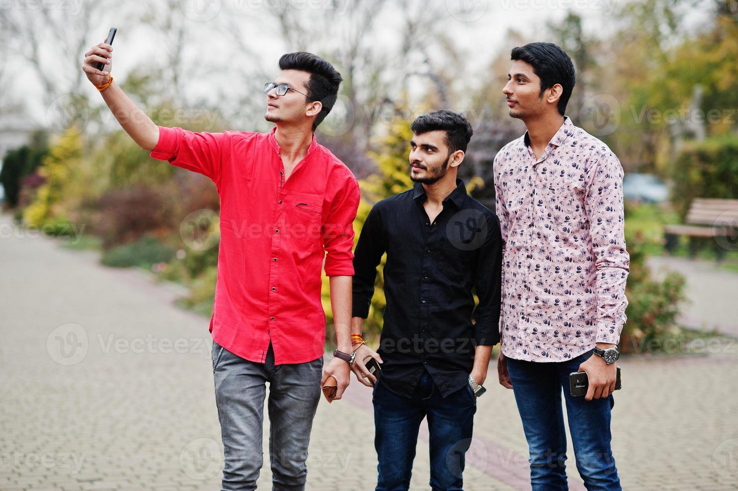 tres amigos estudiantes indios caminando por la calle y se hacen selfie en el teléfono móvil. foto