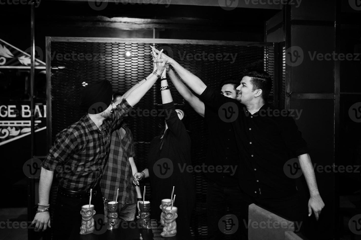 Group of indian friends having fun and rest at night club, drinking cocktails and giving high five together. photo