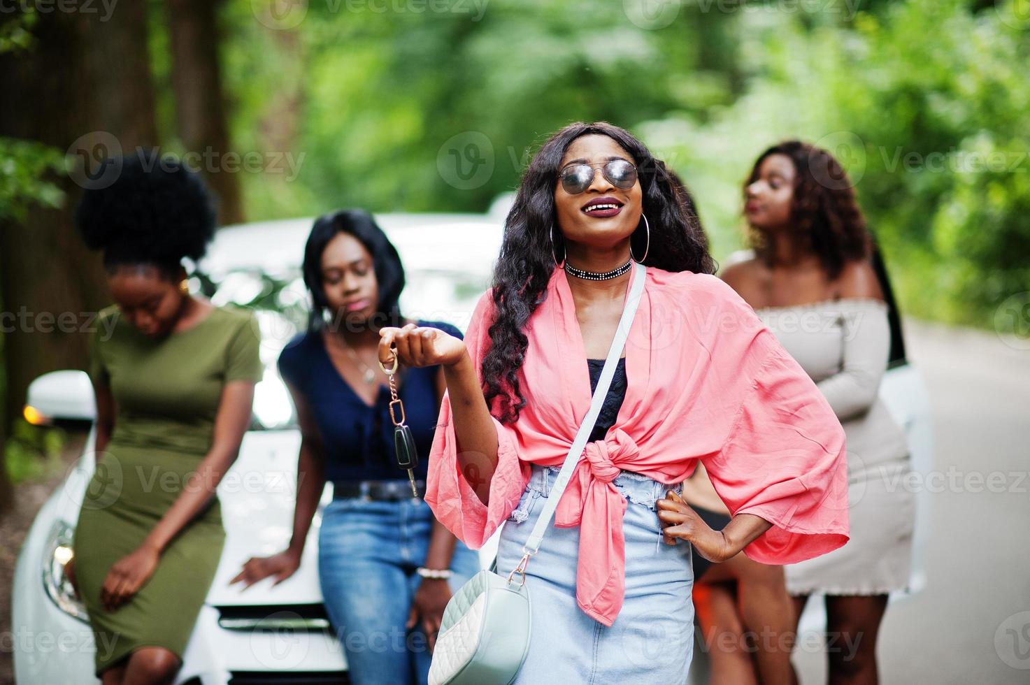 Group of five happy african american girls posed against car, one of them show keys. photo