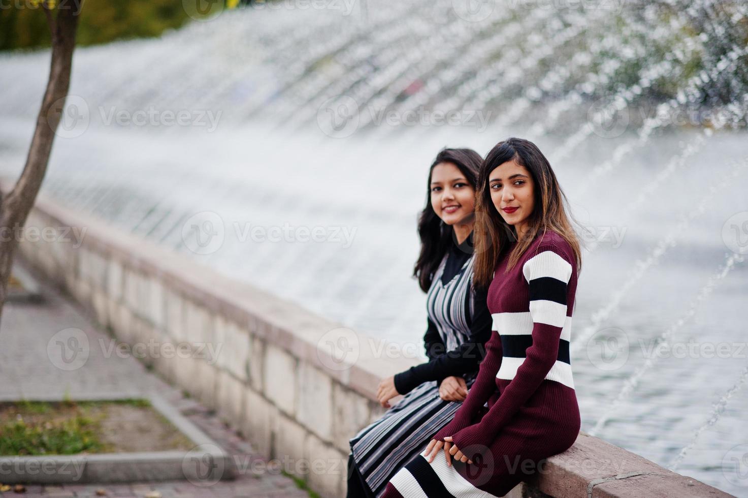 Portrait of two young beautiful indian or south asian teenage girls in dress posed against fountains. photo