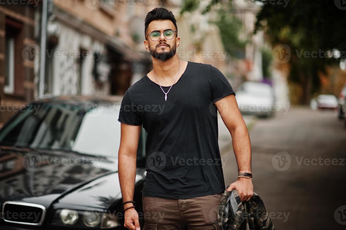 Awesome beautiful tall ararbian beard macho man in glasses and black t-shirt walking against business car. photo