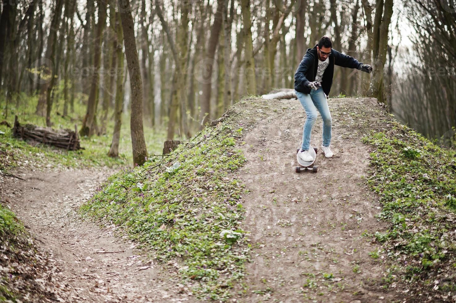 Street style arab man in eyeglasses with longboard on wood. photo
