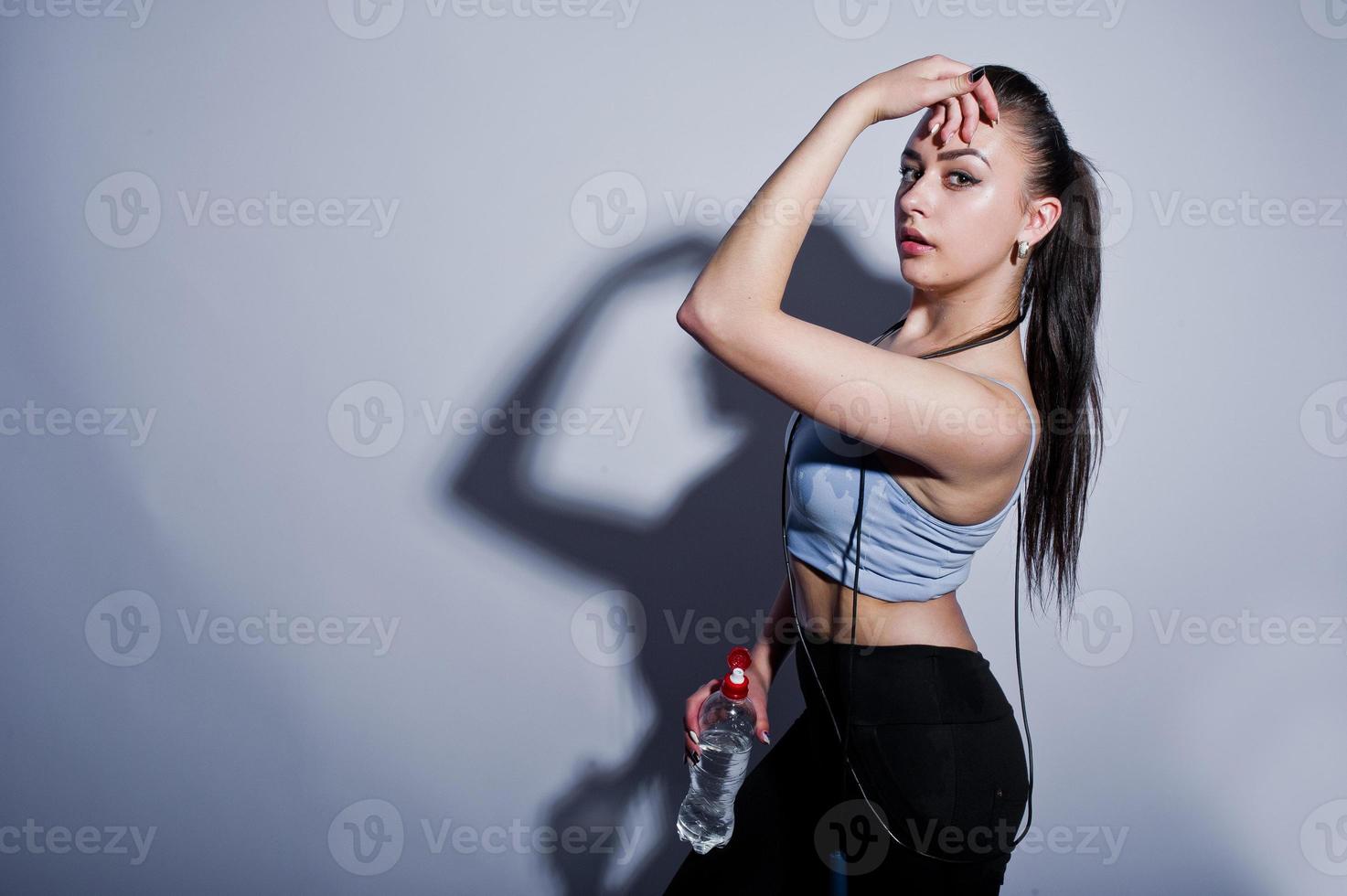 Wet cheerful attractive young fitness woman in top and black leggings with jump rope and bottle of water isolated over white background. photo