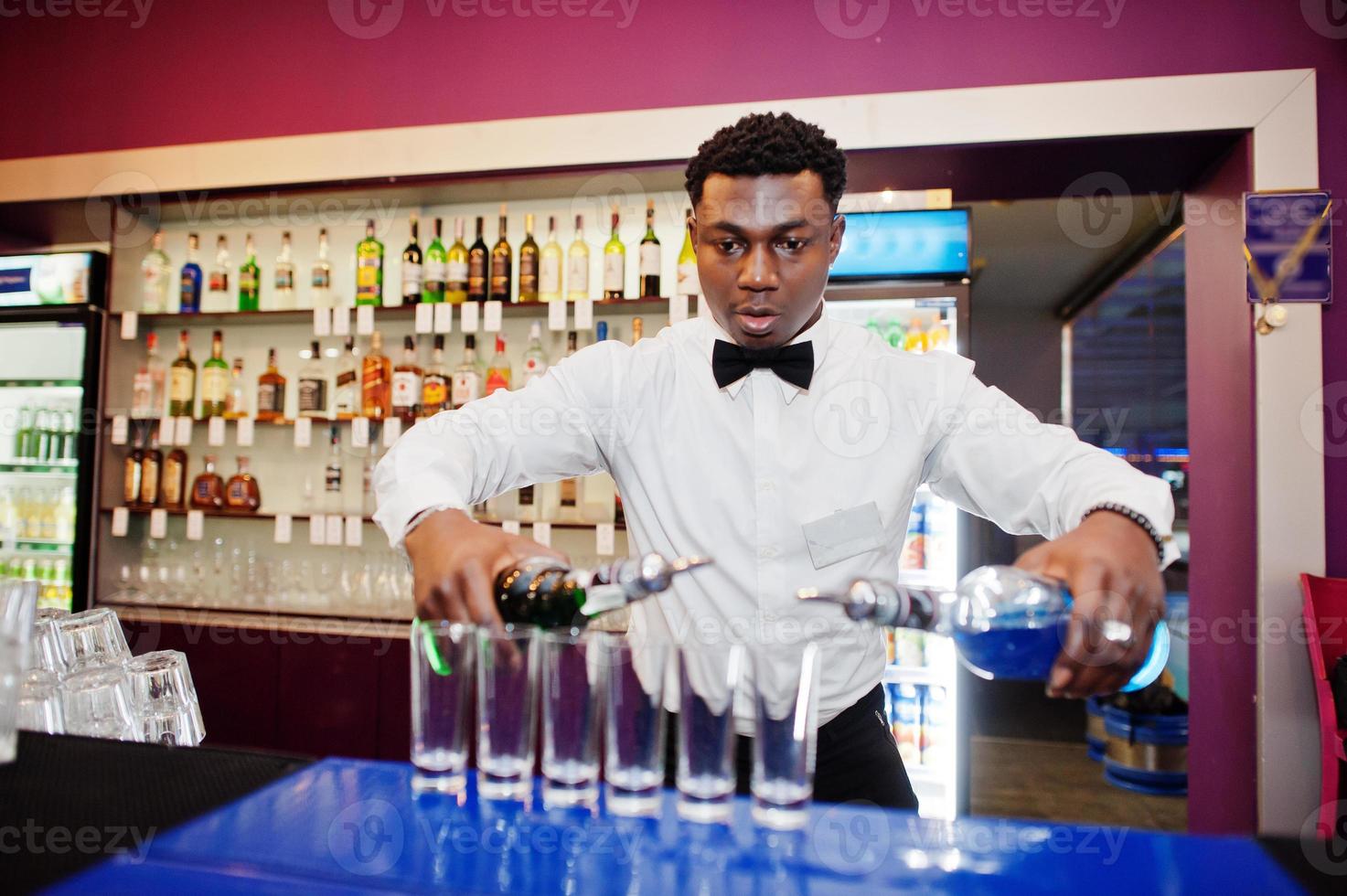 camarero afroamericano en el bar haciendo cócteles en tiros. preparación de bebidas alcohólicas. foto