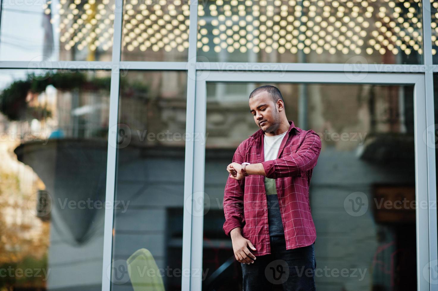 South asian indian male student wear casual posed outdoor and look at his watches. photo