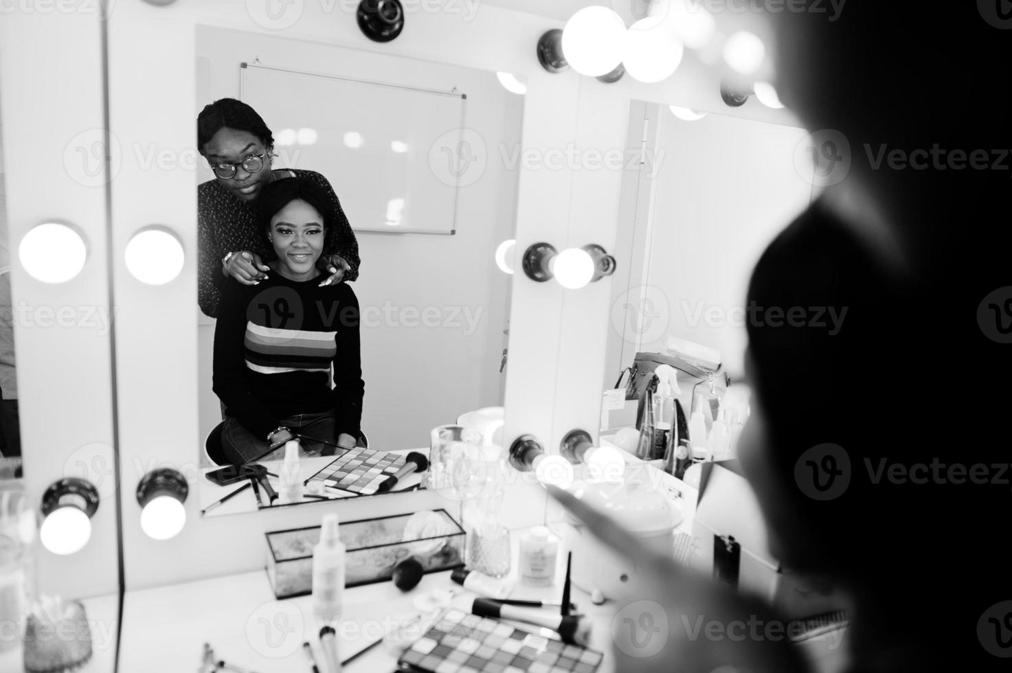 African American woman applying make-up by make-up artist at beauty saloon. photo