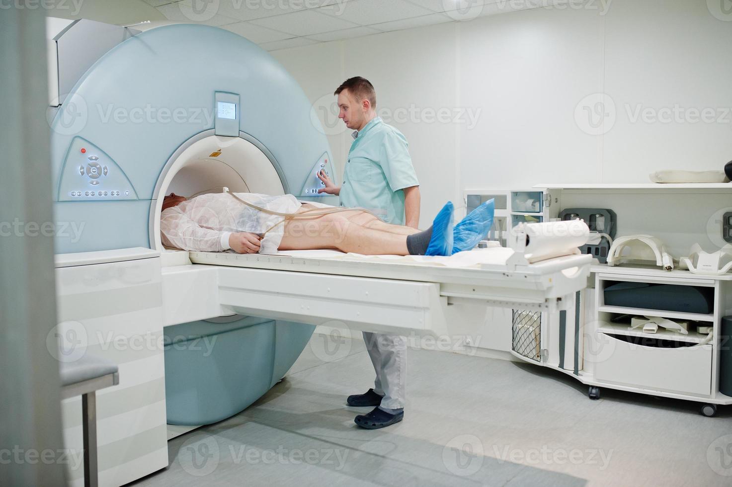 Male doctor turns on magnetic resonance imaging machine with patient inside. photo