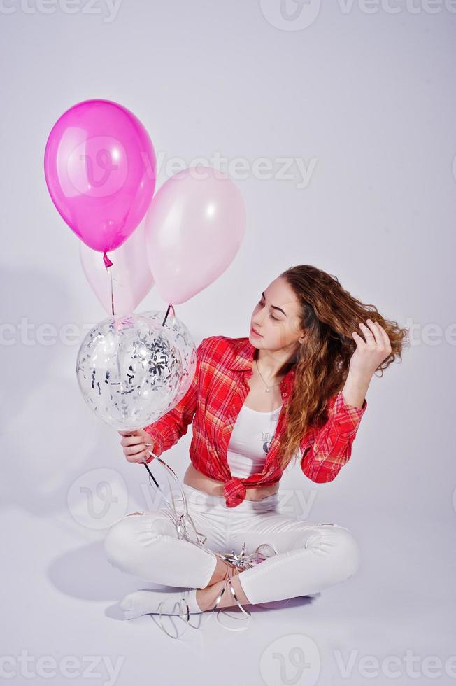 Young girl in red checked shirt and white pants with balloons against white background on studio. photo