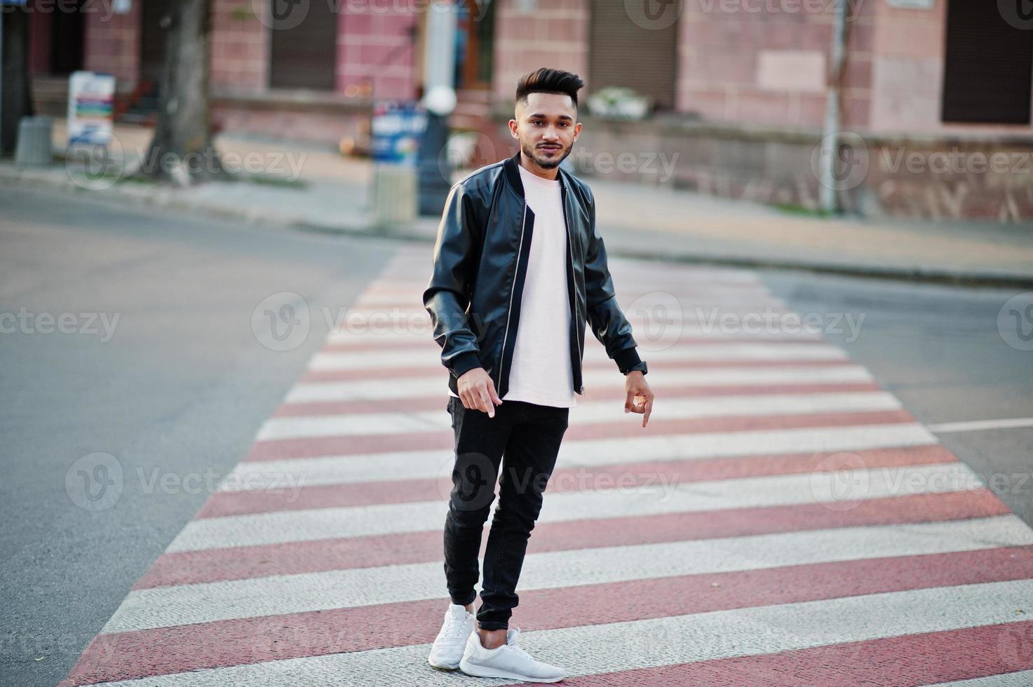 Stylish indian beard man at black leather jacket walking on zebra crossing. India model posed outdoor at streets of city. photo