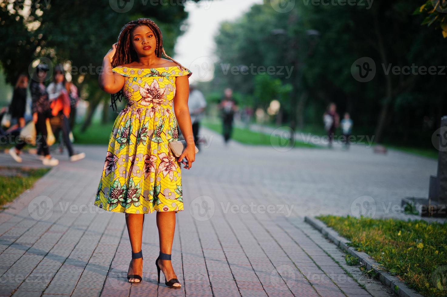 Cute small height african american girl with dreadlocks, wear at coloured yellow dress, posed at sunset. photo