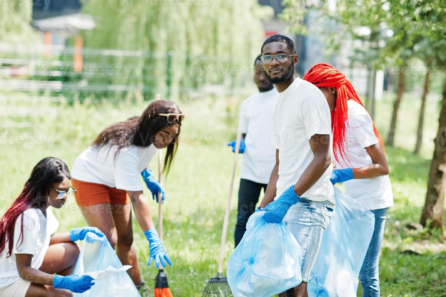 Group of happy african volunteers with garbage bags cleaning area in park. Africa volunteering, charity, people and ecology concept. photo