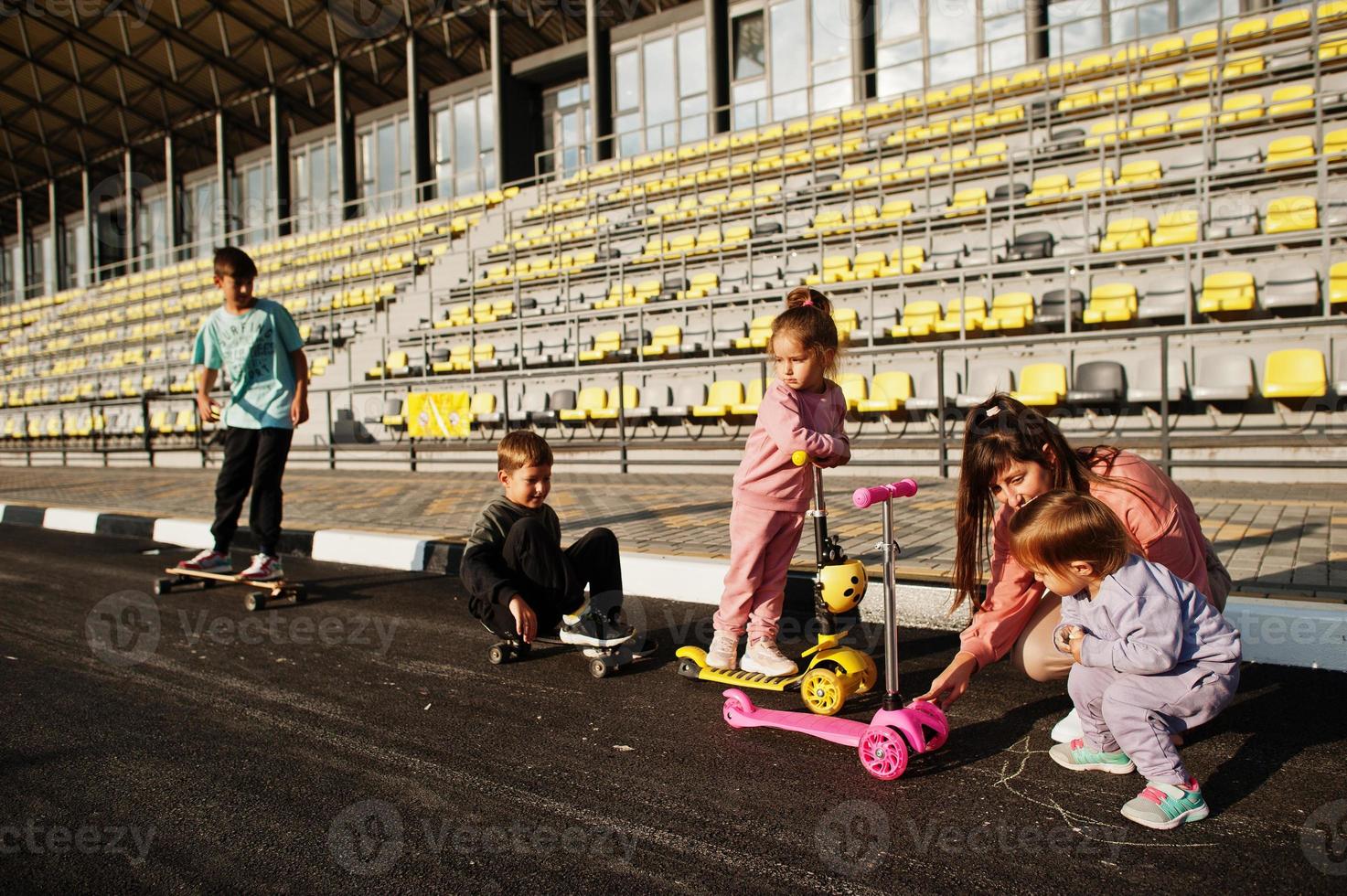 Young stylish mother with four kids outdoor. Sports family spend free time outdoors with scooters and skates. Painted with chalk on the asphalt. photo