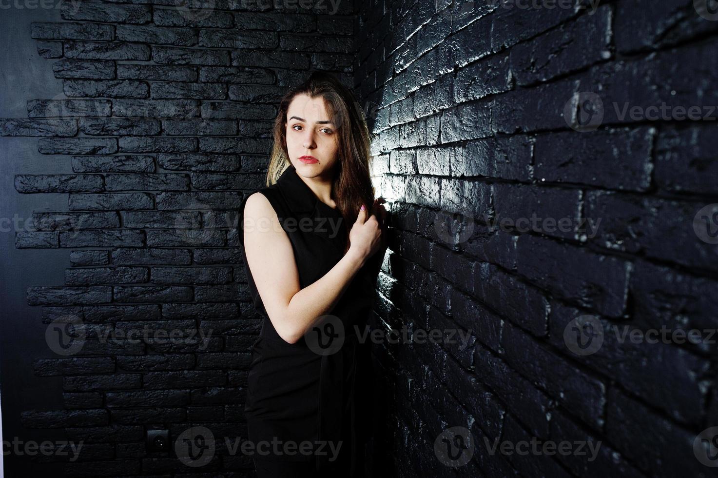 Portrait of a beautiful brunette girl in black jumpsuit in the studio next to the brick wall. photo