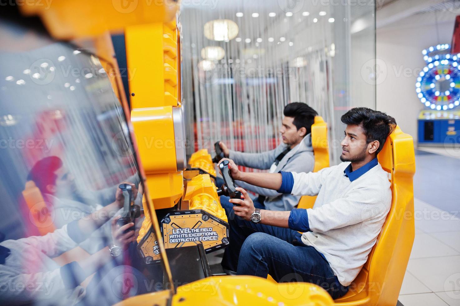 Two asian guys compete on speed rider arcade game racing simulator machine. photo