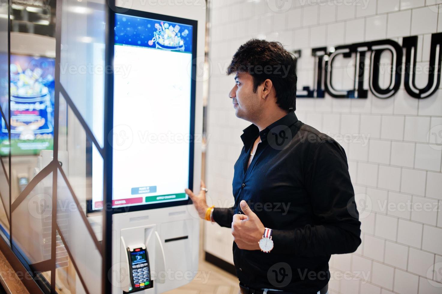 Indian man customer at store place orders and pay through self pay floor kiosk for fast food, payment terminal. He show thumb up. photo