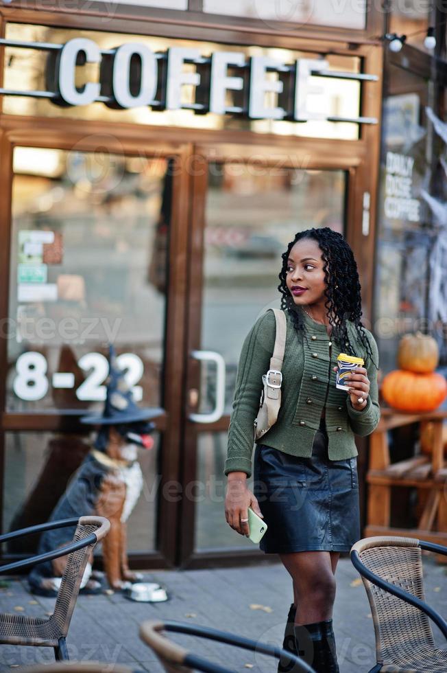 elegantes mujeres afroamericanas con verde y falda negra posaron en un café al aire libre con una de café y hablaron por teléfono móvil. 10487699 Foto de stock