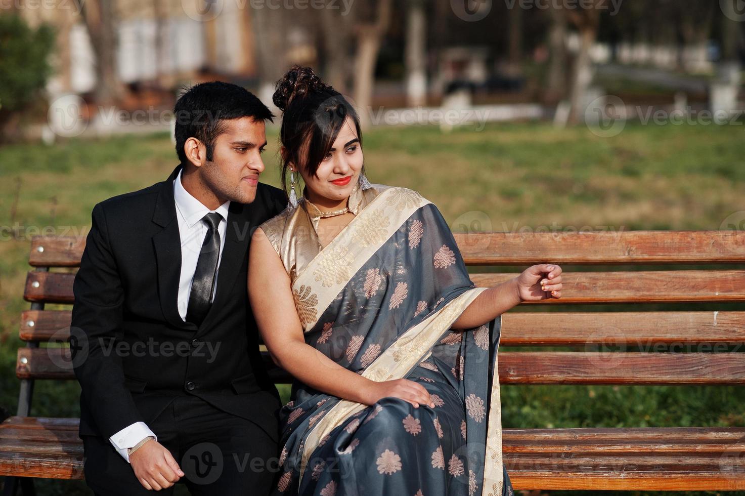 Elegant and fashionable indian friends couple of woman in saree and man in suit sitting on bench. photo