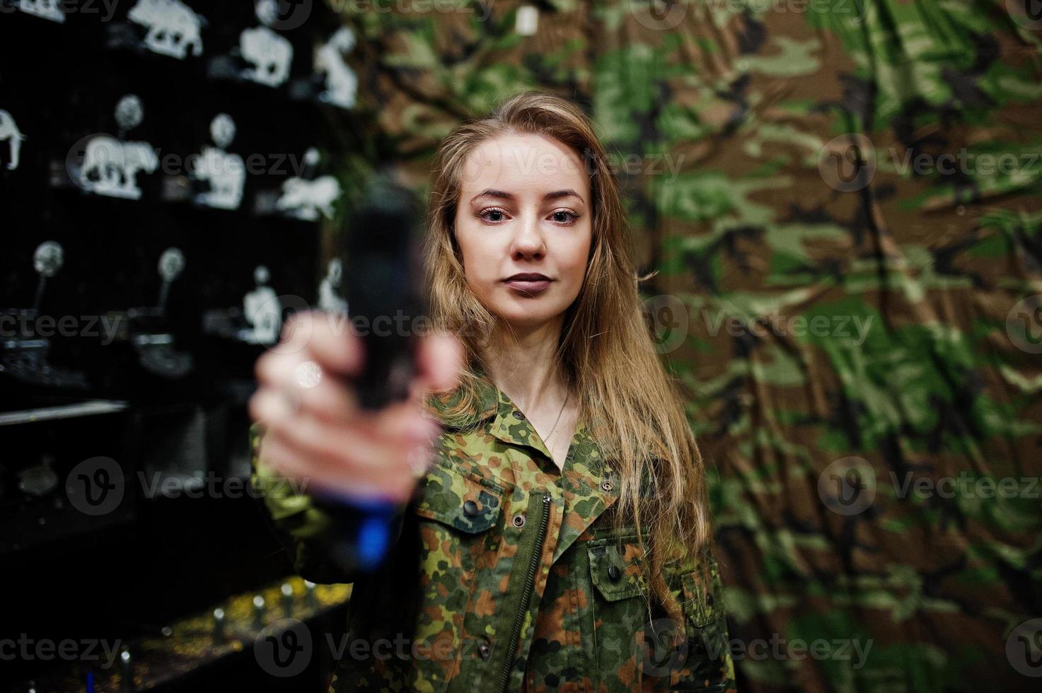 Military girl in camouflage uniform with gun at hand against army background on shooting range. photo