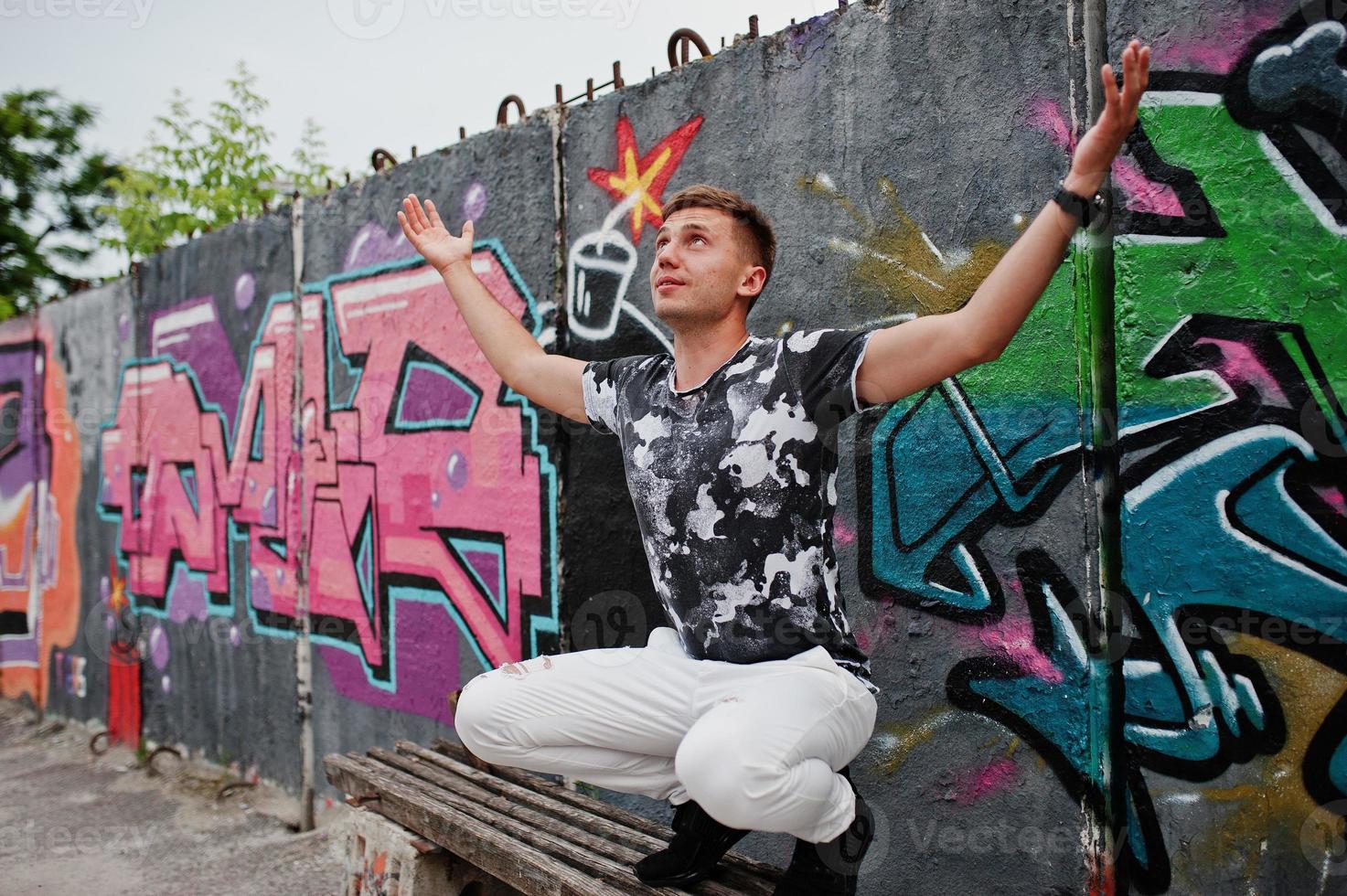 Lifestyle portrait of handsome man posing on the street of city with graffiti wall. photo