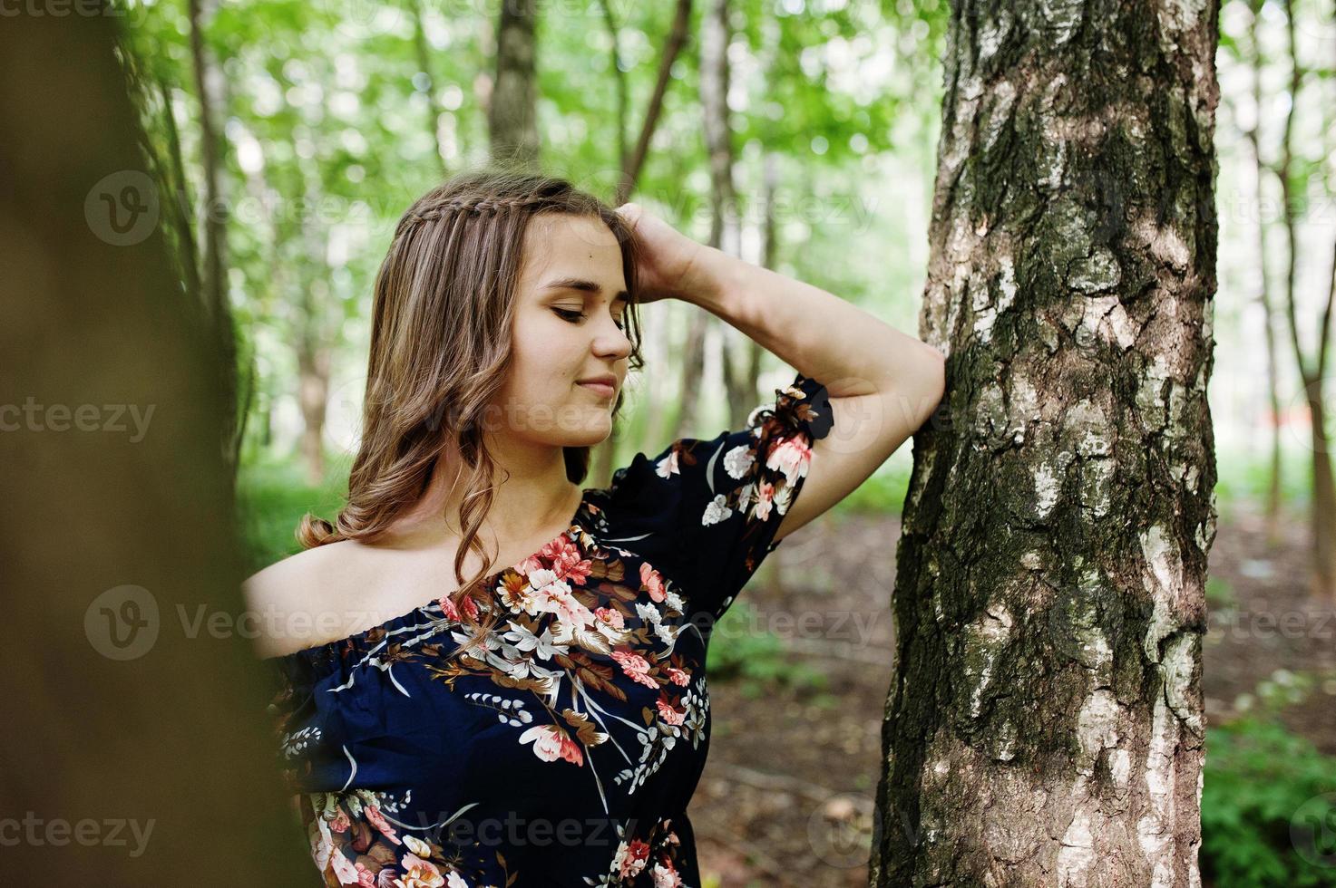 Portrait of a fabulous young girl in pretty dress with stylish curly hairstyle posing in the forest or park. photo