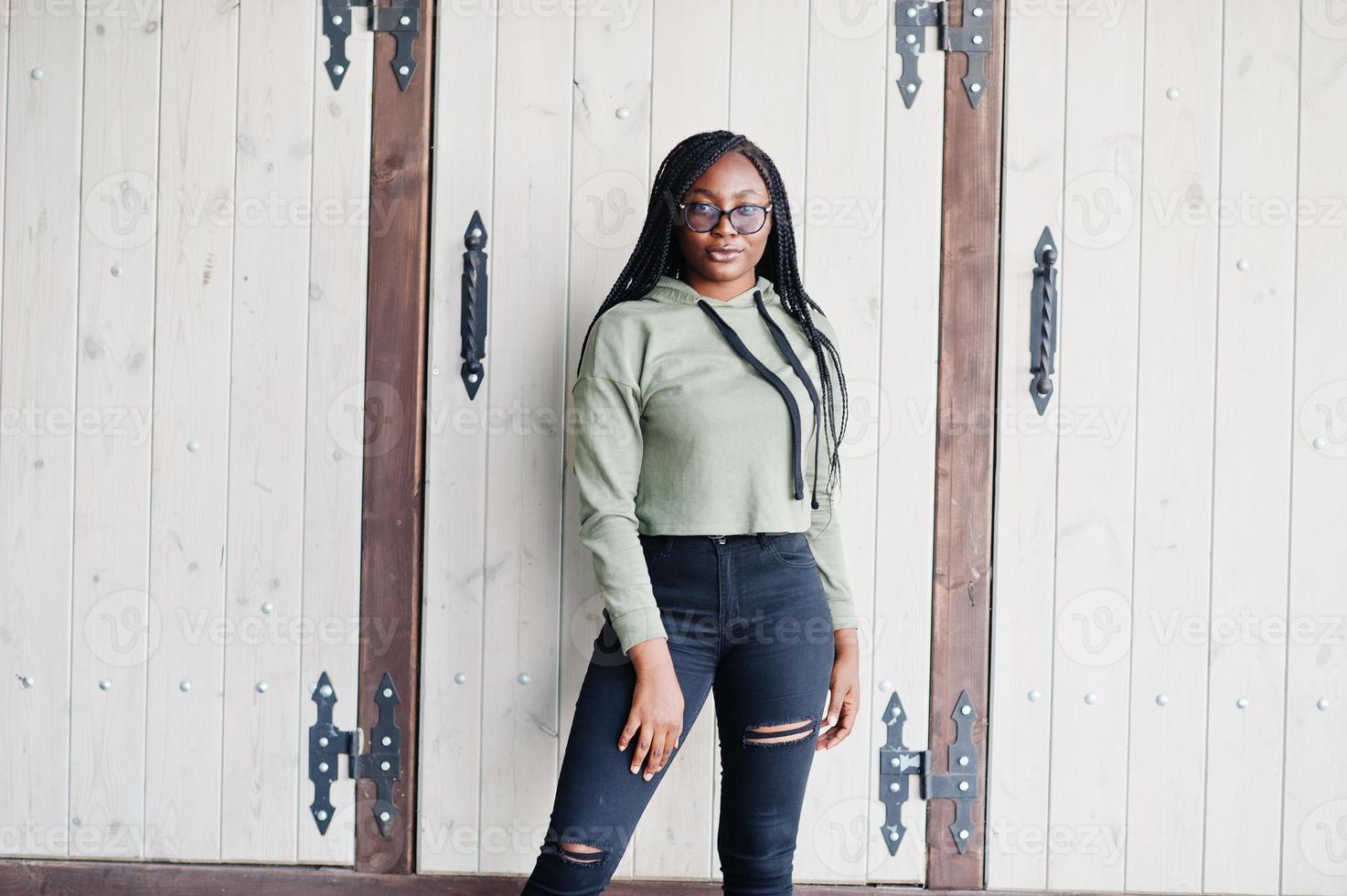 City portrait of positive young dark skinned female wearing green hoody and eyeglasses. photo