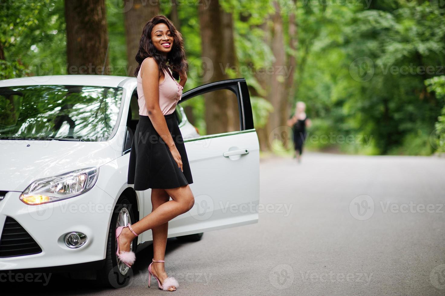 mujer afroamericana posó contra un auto blanco en un camino forestal. foto