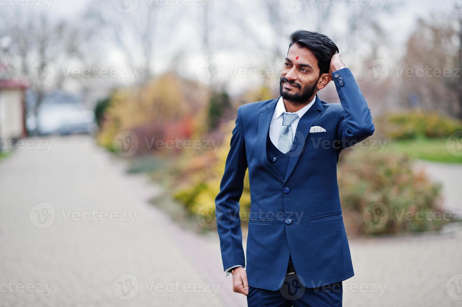 Stylish beard indian man with bindi on forehead, wear on blue suit posed outdoor. photo