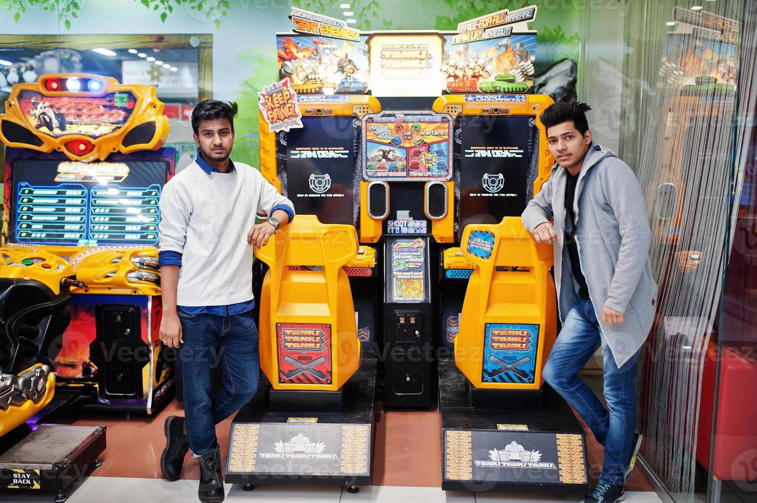 Two asian guys compete on speed rider arcade game racing simulator machine. photo