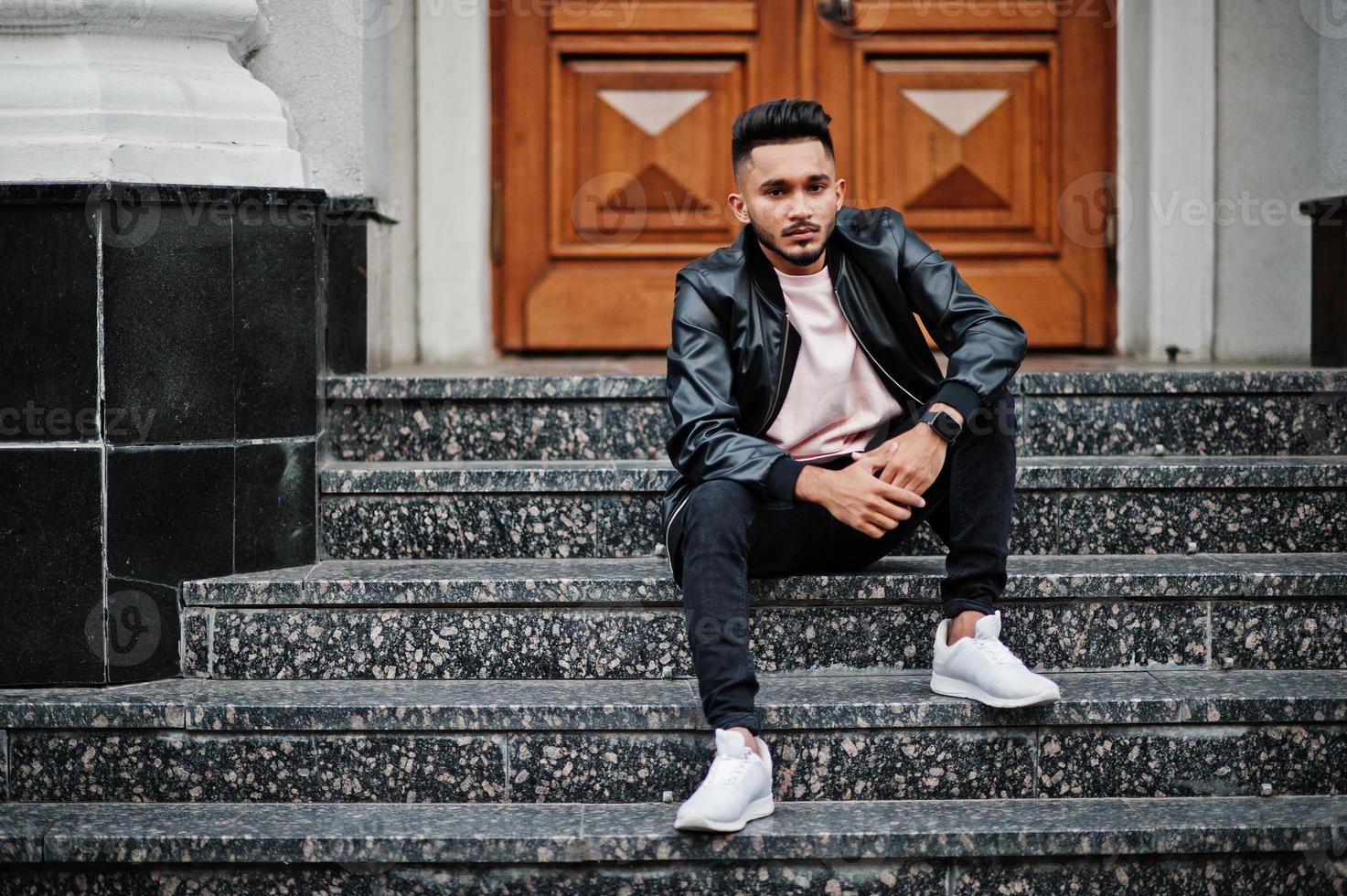 Stylish indian beard man at black leather jacket. India model posed sitting at streets of city. photo