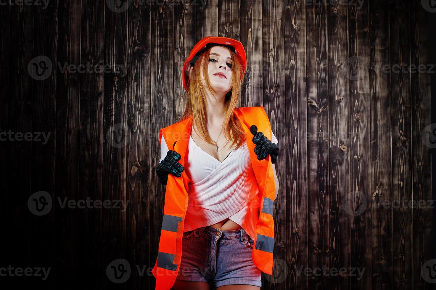 Engineer woman in orange protect helmet and building jacket against wooden background. photo