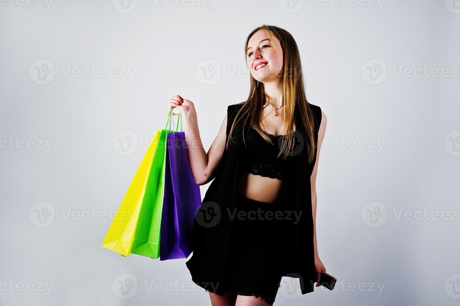 Girl model in black wear with colored shopping bags posed at studio on white background. photo