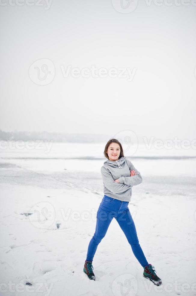 Funny girl wear on hoody sweater and jeans, at frozen lake in winter day. photo