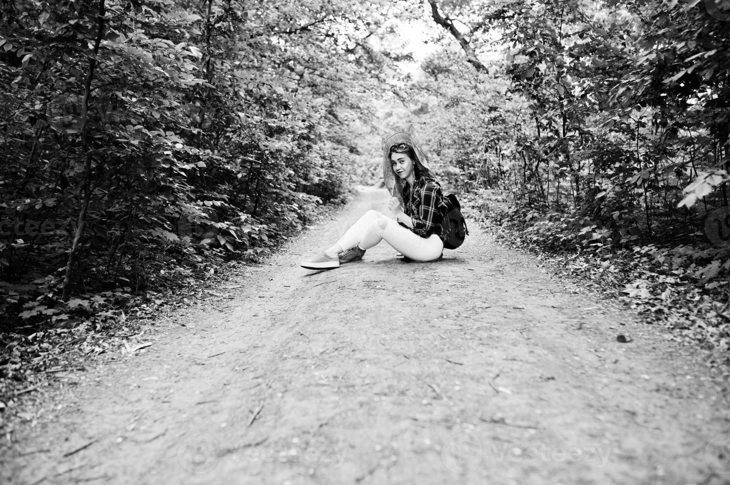 Portrait of a positive young gorgeous blonde sitting on the ground with a map in her hands in the forest. photo