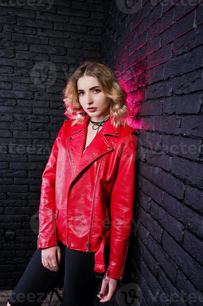 Studio portrait of blonde girl in red leather jacket against brick wall. photo