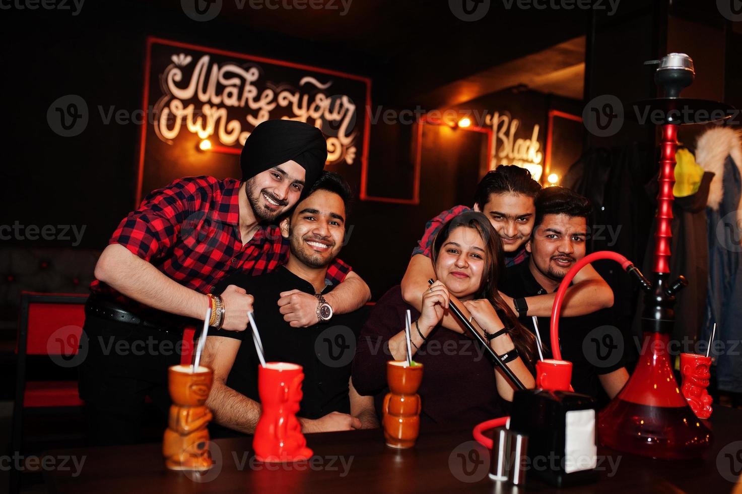 grupo de amigos indios divirtiéndose y descansando en el club nocturno, bebiendo cócteles y fumando narguile. foto