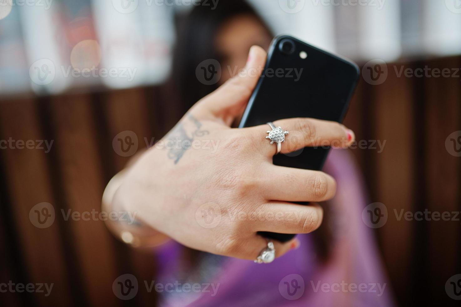 Indian hindu girl at traditional violet saree sitting at cafe table with mobile phone at hands, making selfie. photo