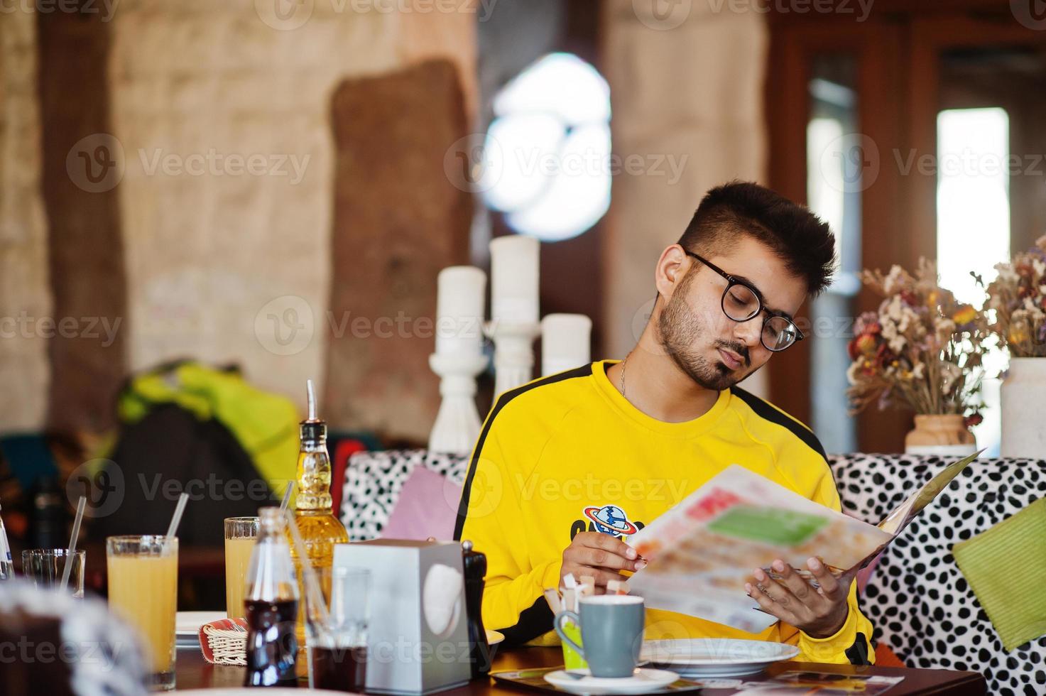 Asian man in eyewear and yellow sweatshirt sitting in cafe and read menu. photo