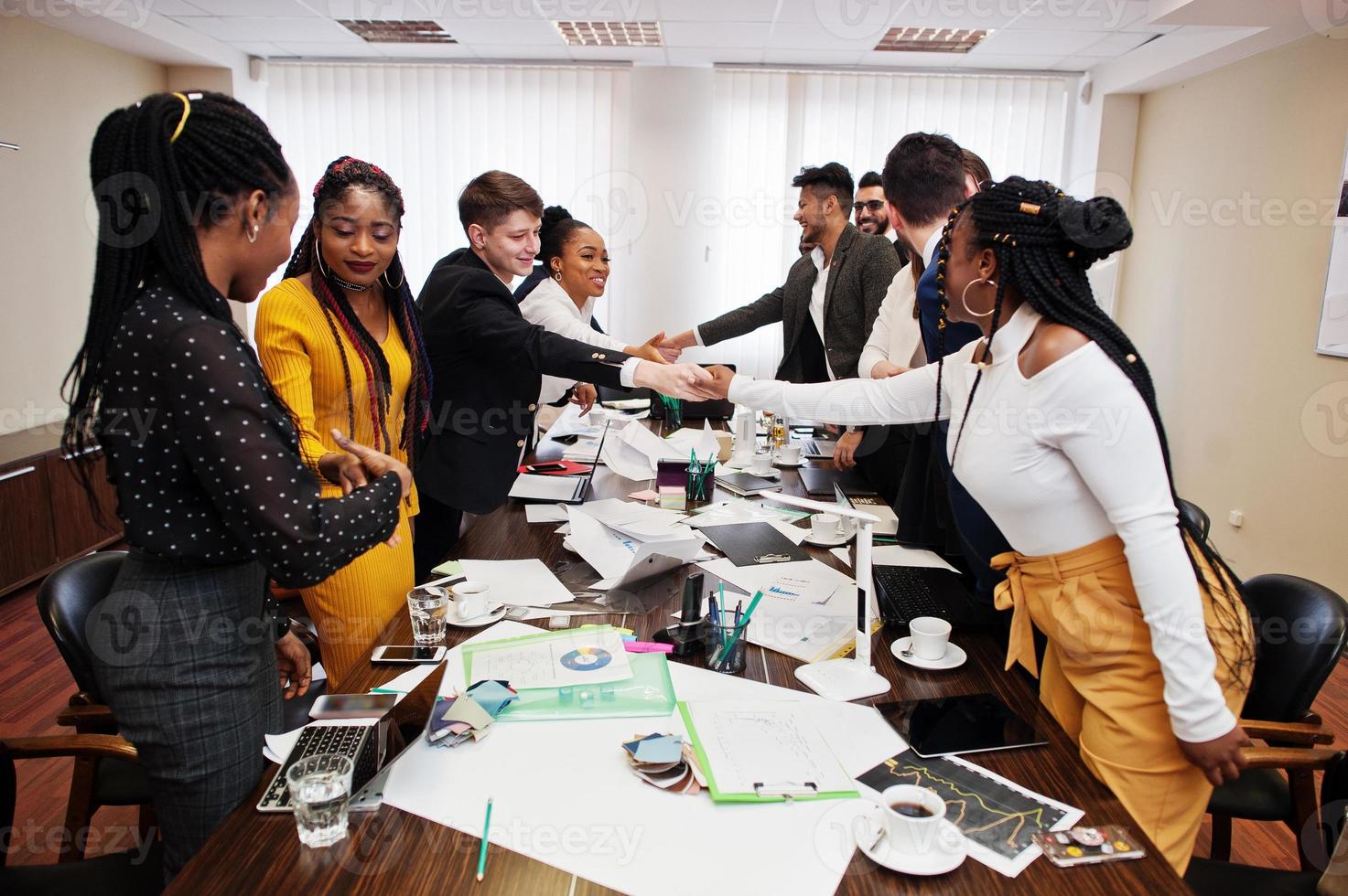 Good deal. Multiracial business team addressing meeting around boardroom table and shaking hands each other. photo