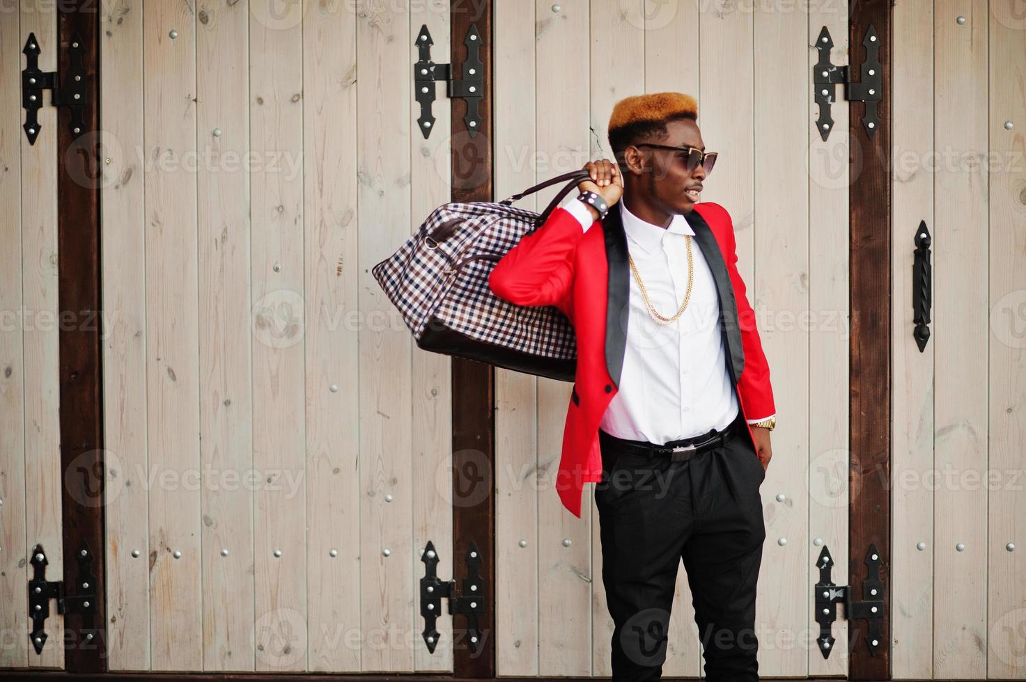 modelo de hombre afroamericano de moda en traje rojo, con cabello destacado y bolso posado en la calle. foto