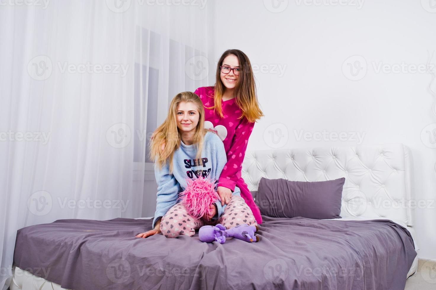 Two friends girls in pajamas having fun on bed at room. photo