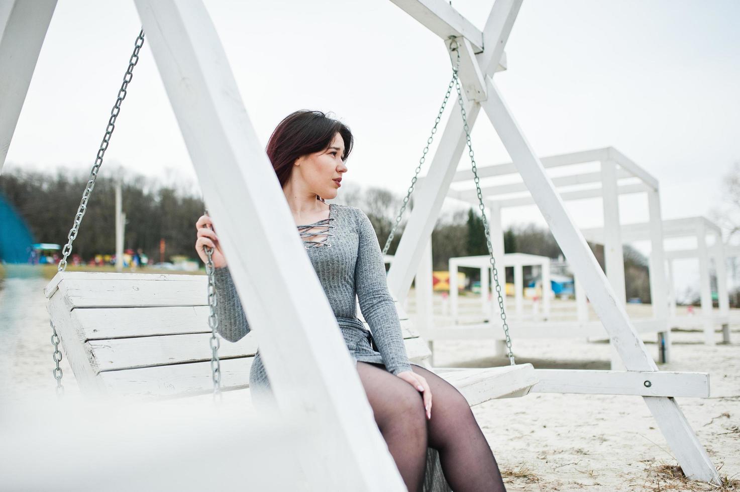 Portrait of brunette girl in gray dress sitting at white wooden construction. photo